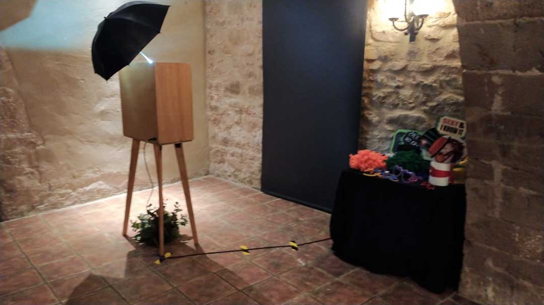 Fotomatón de madera en un sótano de boda con paredes de piedra y fondo negro en una finca de Valencia.