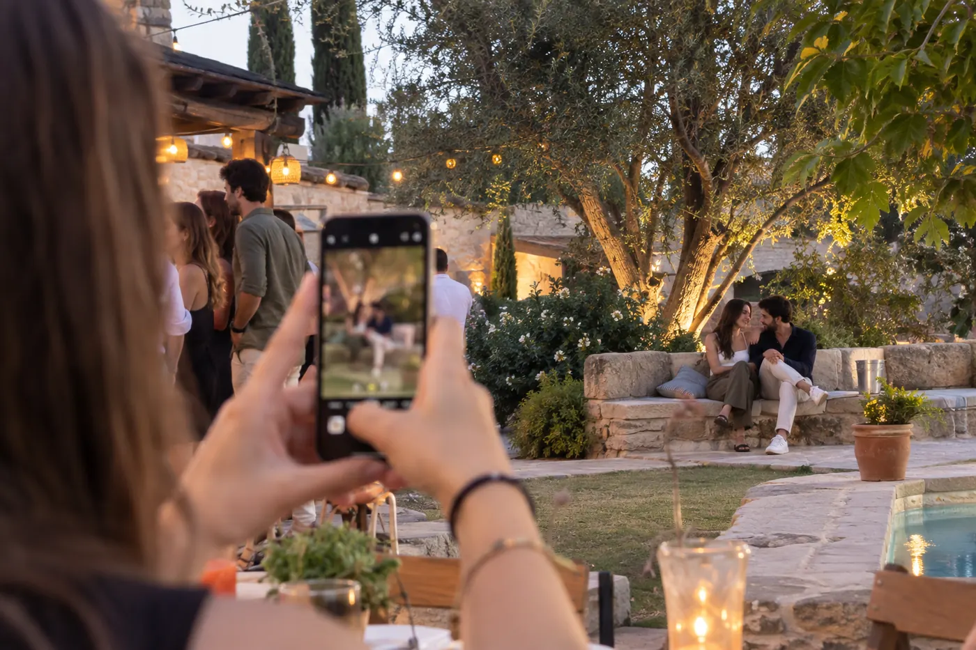 Una invitada fotografía con el móvil a una pareja sentada en el jardín durante una boda